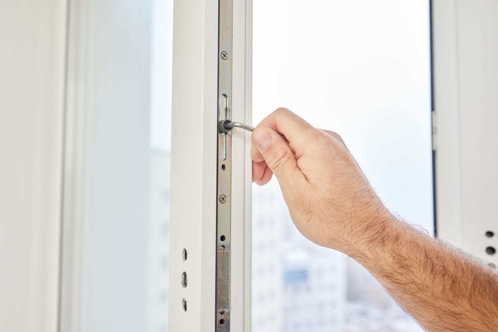 Handwerker stellt mit einem Schraubendreher den Beschlag eines Kunststofffensters nach
